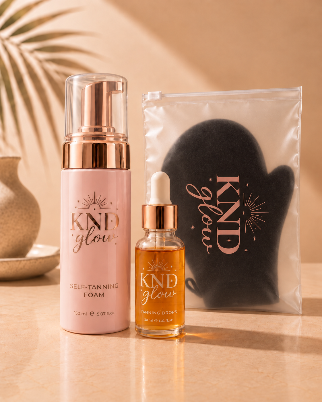 Kind Glow self-tanning foam bottle, tanning drops bottle, and black applicator mitt displayed together on a beige surface.