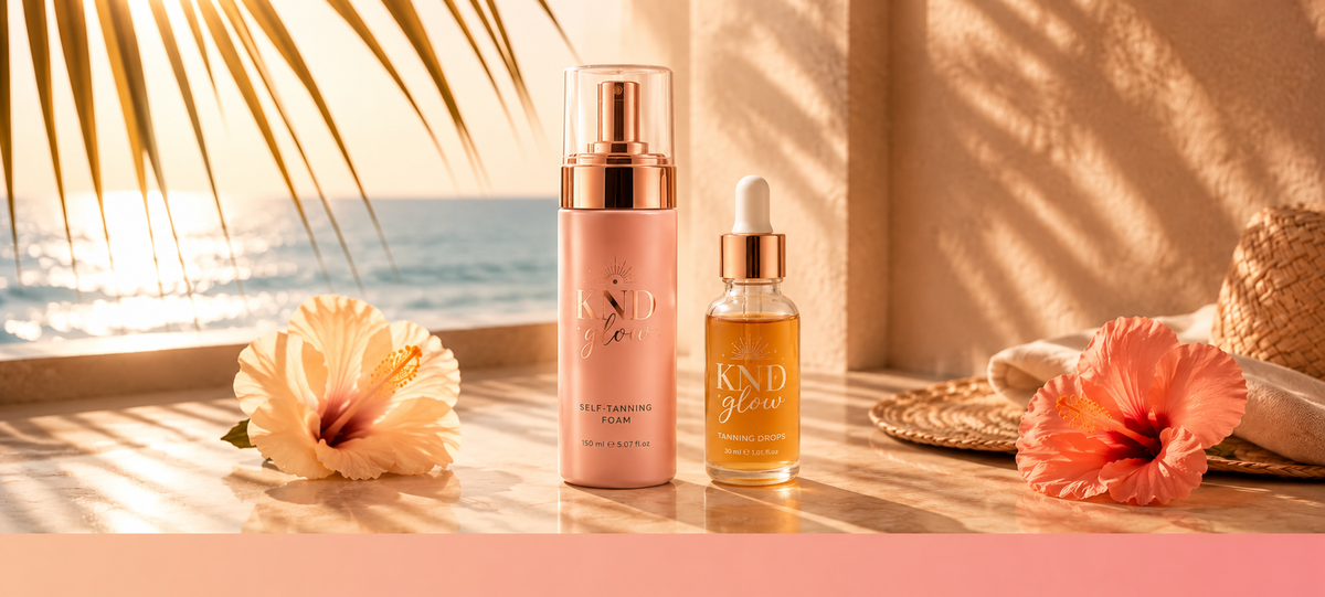 Kind Glow self tanning foam and tanning drops displayed beside hibiscus flowers by the sea.